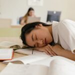 Student asleep at a desk surrounded by books after studying