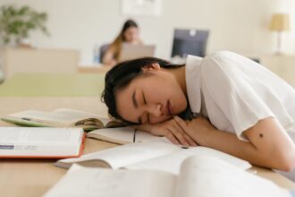 Student asleep at a desk surrounded by books after studying