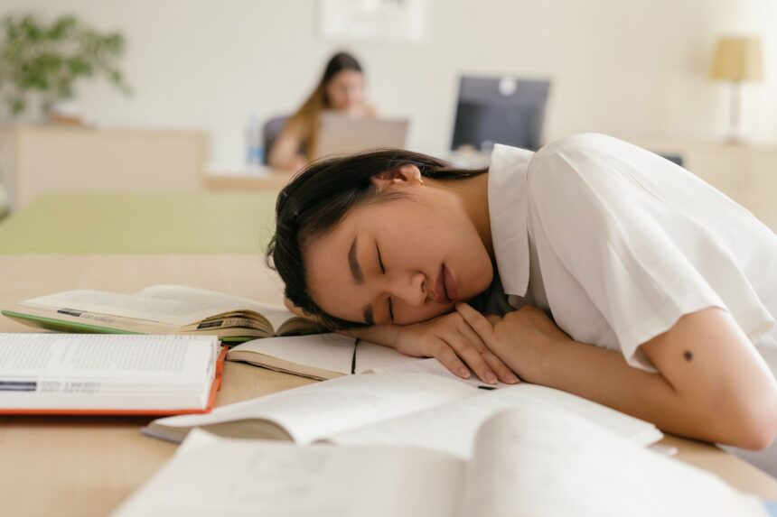 Student asleep at a desk surrounded by books after studying